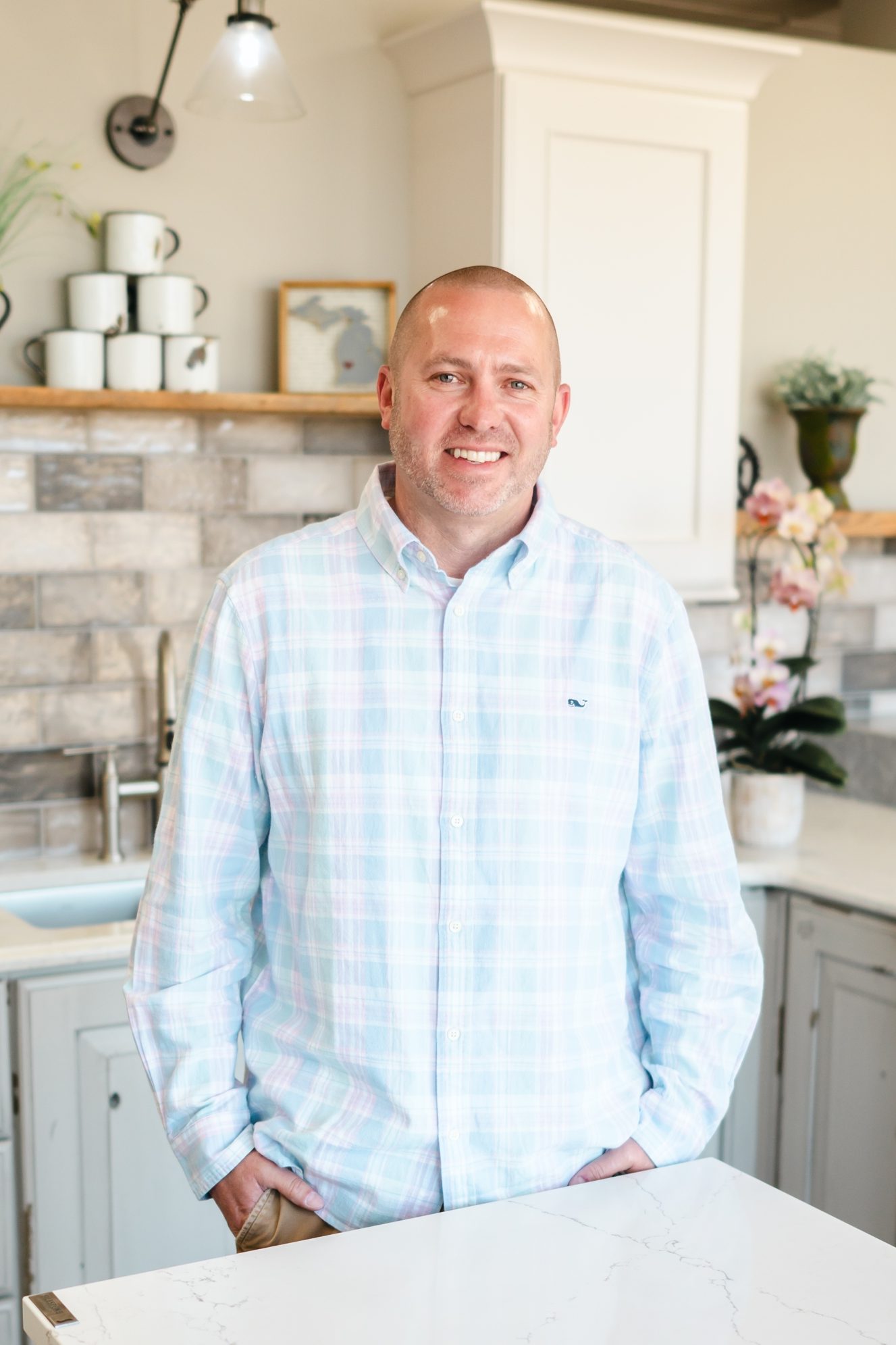 man standing in a kitchen wearing a button up and smiling