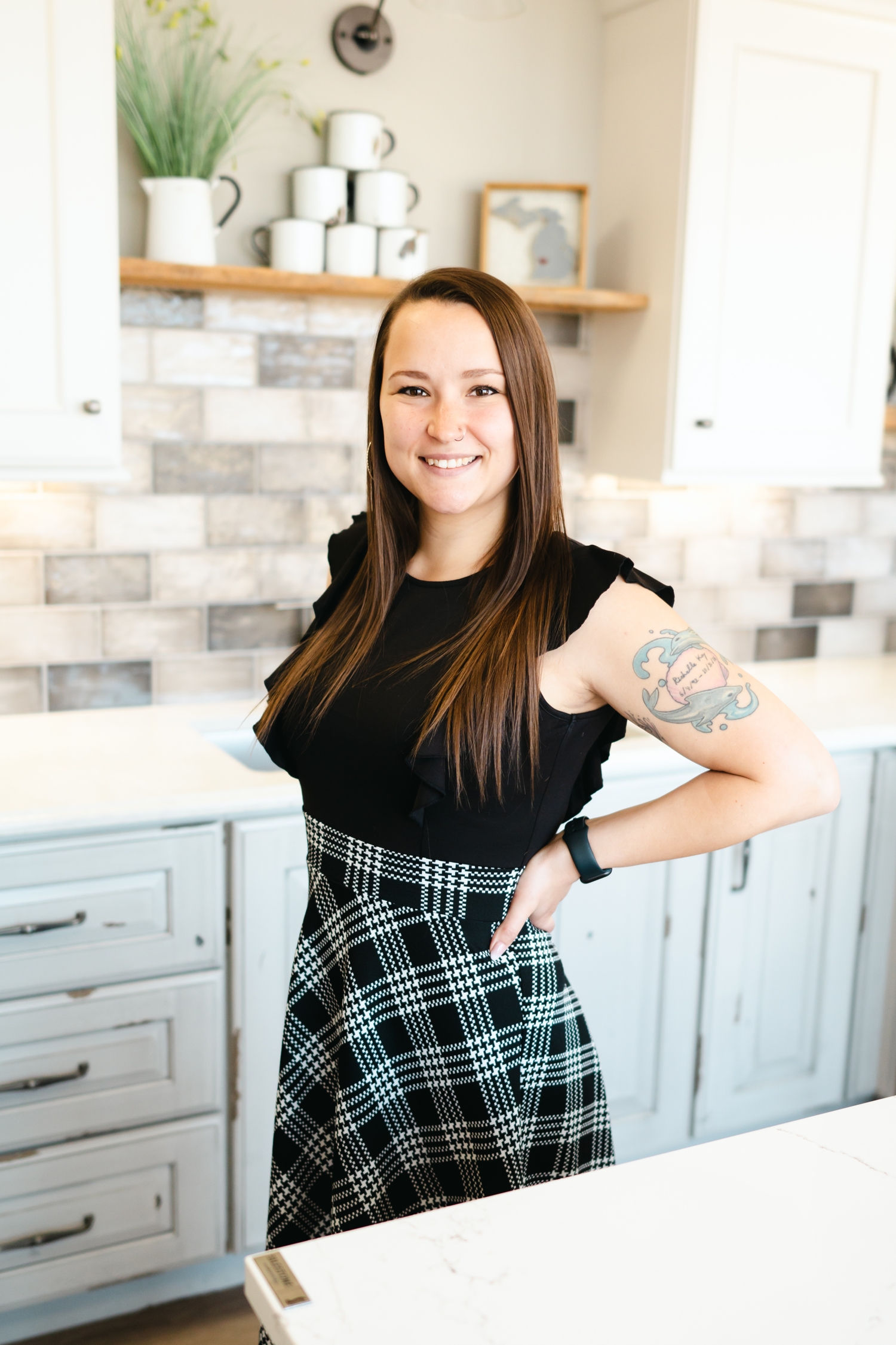 a smiling young woman with her hands on her hips wearing a black plaid dress